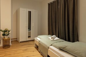 Un dormitorio con cama, armario, una mesita redonda con una planta y una cortina.
