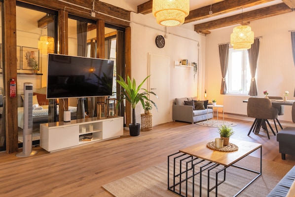 Una sala de estar moderna con un televisor de pantalla plana, piso de madera, un sofá, una mesa de centro y un comedor con una silla.