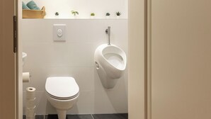 Moderni kylpyhuone, jossa on wc, pissaari ja pieni hylly, jossa on kasveja.