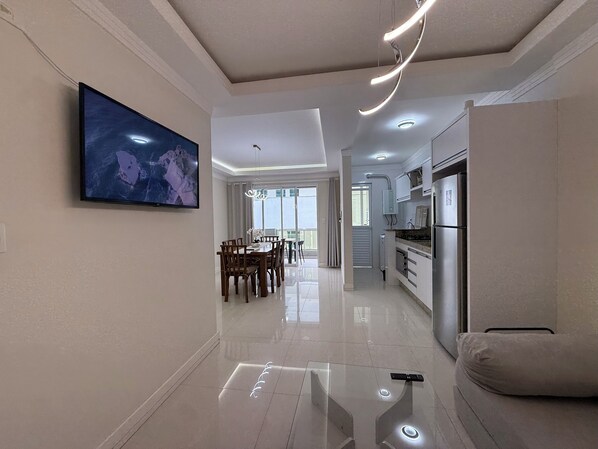 A modern kitchen with stainless steel appliances, a dining area with a table and chairs, and a large flat-screen TV mounted on the wall. - Exclusive apartment 50 meters from the sea (Bombinhas)