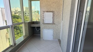 Un balcon doté d’un sol carrelé, d’un plafond en bois et offrant une vue sur des immeubles et des arbres.