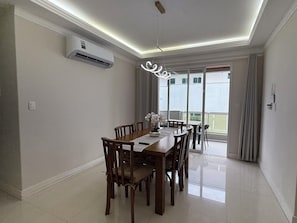 A dining area with a wooden table and chairs, an air conditioning unit, and a view through a glass door. - Exclusive apartment 50 meters from the sea (Bombinhas)