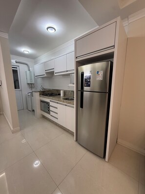 A modern kitchen with white cabinets, a stainless steel refrigerator, and a built-in oven. - Exclusive apartment 50 meters from the sea (Bombinhas)