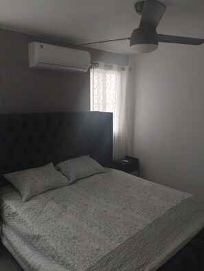 Ein Schlafzimmer mit einem Bett, einem Nachttisch, einer Klimaanlage und einem Deckenventilator.