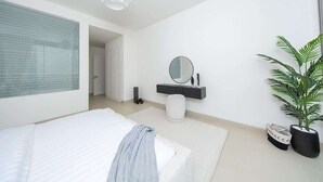 Ein modernes Schlafzimmer mit einem Bett, einem Nachttisch, einem Spiegel, einer Topfpflanze und einem Fenster mit Jalousien.
