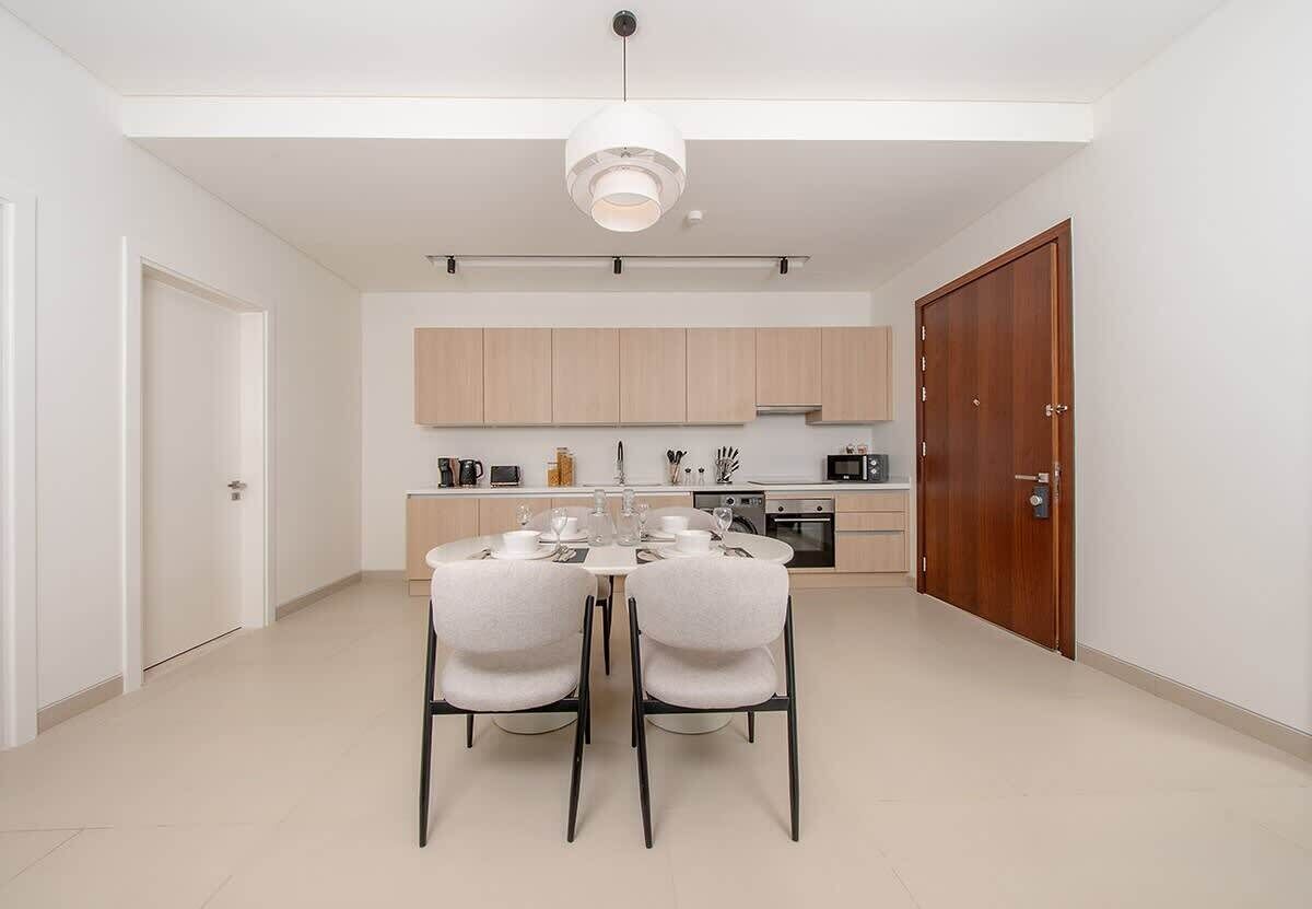 A modern kitchen with wooden cabinets, a dining table with chairs, and a pendant light.