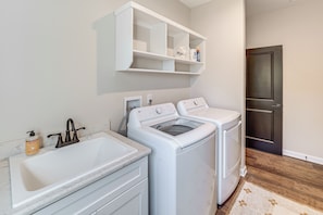 A laundry area with a sink, two washing machines, and a shelf above.