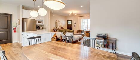 A modern kitchen with a large island, dining area with a wooden table and chairs, and a living room with a sofa and coffee table.