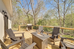 A deck with wooden chairs, a grill, and a fire pit.