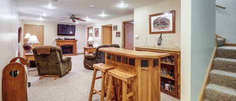 A living room with a fireplace, a TV, and a bar area with stools.