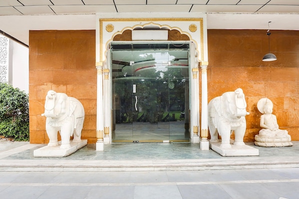LâentrĂ©e dâun bĂątiment est ornĂ©e dâune porte en verre, flanquĂ©e de deux statues dâĂ©lĂ©phants et dâune statue de Bouddha assis.