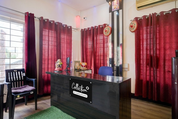 Un mostrador de recepción con un letrero, una silla y una silla de oficina azul, junto con cortinas rojas.