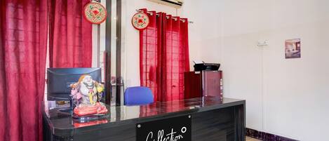 Un mostrador de recepción con un cartel que dice 'Collection Company-Serviced', cortinas rojas, una silla azul y un aire acondicionado montado en la pared.