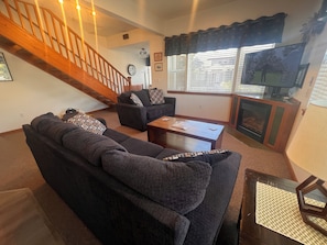 Ein Wohnzimmer mit einer Couch, einem Couchtisch und einem Kamin. Im Hintergrund ist eine Treppe zu sehen.