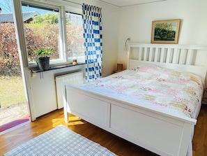 A bedroom with a white bed, a window with a view of the outdoors, a radiator, and a small table with a lamp. - 5 Person Holiday Home in Ronneby (Ronneby)