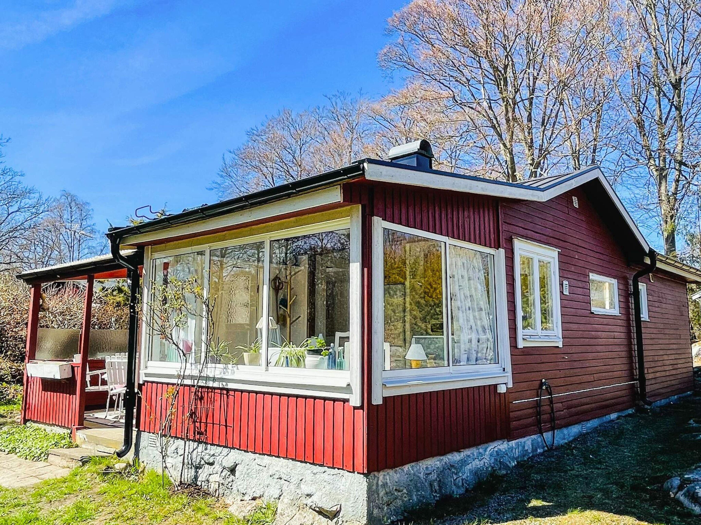 A red wooden cabin with large windows, a covered porch, and a small outdoor seating area.