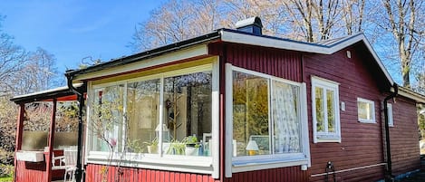 A red wooden cabin with large windows, a covered porch, and a small outdoor seating area.