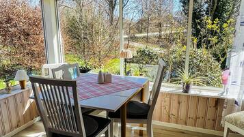 A conservatory with a table and chairs, large windows, and a view of the surrounding garden.