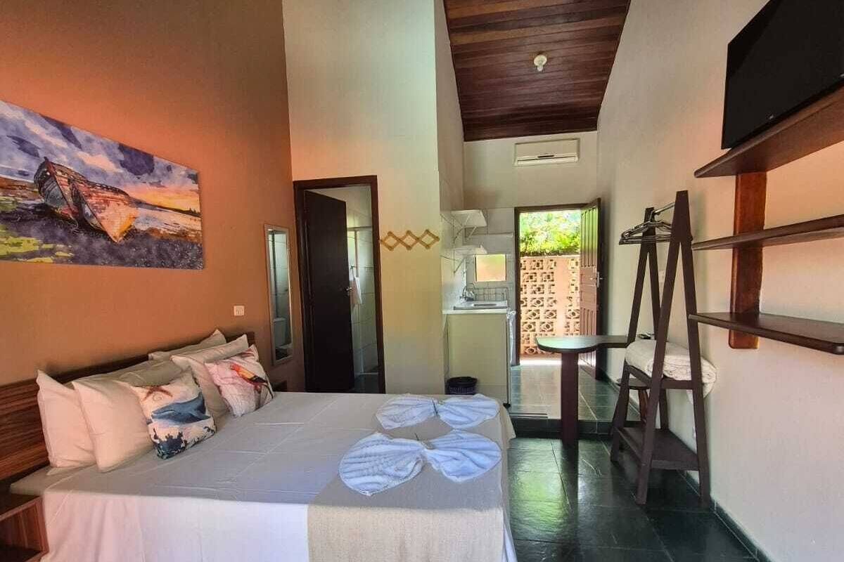 Un dormitorio con una cama, almohadas, un cuadro, una escalera de madera y un baño visible a través de una puerta abierta.