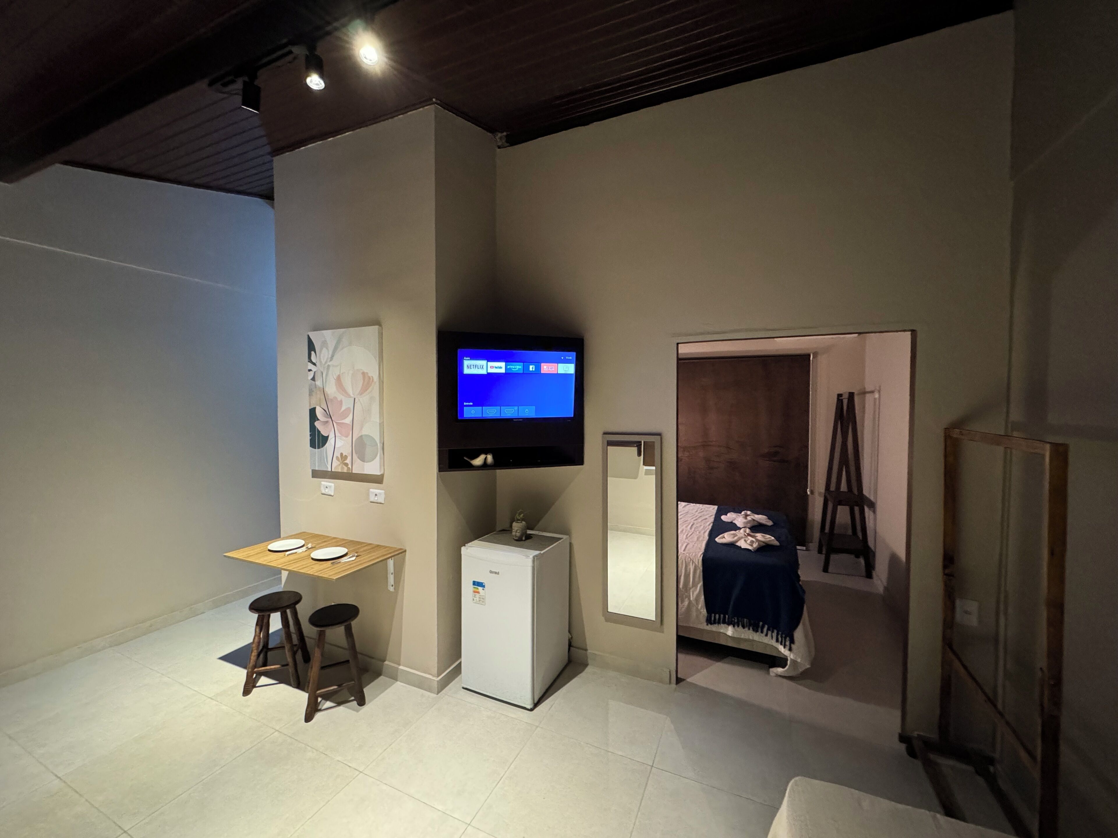A hotel room with a bed, a desk with a computer, a TV mounted on the wall, and a mirror.