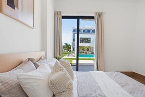 A hotel room with a bed, a view of a swimming pool, and a modern building in the background. - Downtown you can walk to coco bongo Hard rock plazas IKEA and San Juan plaza. (Punta cana)