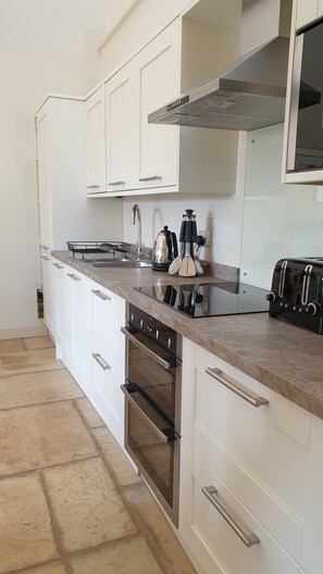 A modern kitchen with white cabinets, a stainless steel range hood, a built-in oven, and a toaster. - Charming Stone Cottage, Perfect for Country Walks or Cycling….Very Dog Friendly! (Martock)
