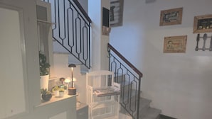 Uma escada com corrimão de metal, uma cadeira branca e uma pequena mesa com abajur e plantas.