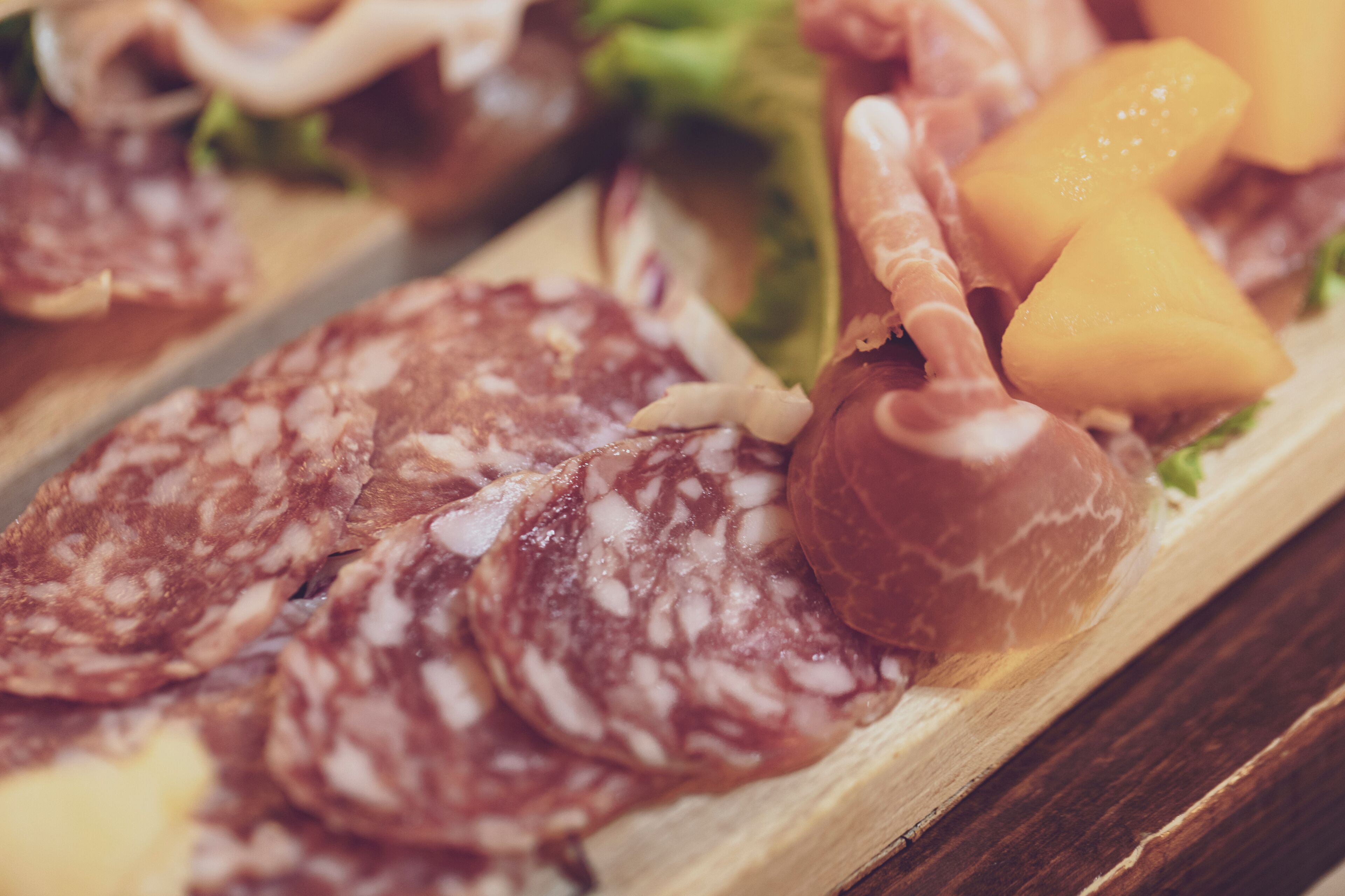 A wooden board with various cured meats and a small piece of cheese.
