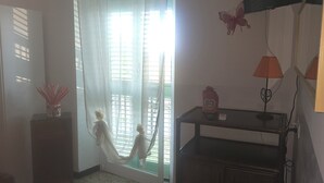 Quarto com porta de correr de vidro, televisão de tela plana na parede, uma mesa pequena com abajur e uma borboleta decorativa na parede.