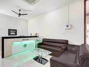 A reception area with a reception desk, a ceiling fan, a wall-mounted air conditioner, and a brown leather sofa.