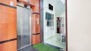 Um elevador com uma placa indicando '1º Andar', uma placa de 'Proibido Fumar' e uma porta de vidro com puxador de metal.