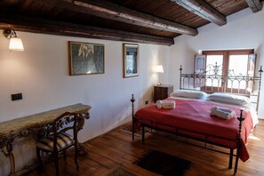 Ein Schlafzimmer mit einem hölzernen Bett, einem Schreibtisch mit Stuhl, einem Fenster mit Blick und einem Gemälde an der Wand.