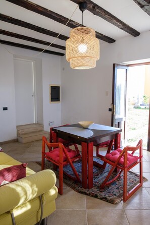 Ein Zimmer mit Esstisch, roten Stühlen, einem gelben Sofa, einer Hängeleuchte aus Weidwerk und einer Tür, die nach draußen führt.