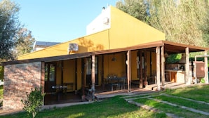 A yellow building with a covered patio, brick walls, and a small garden area. - Jupiter's Dreams House With Private Pool (Syracuse)