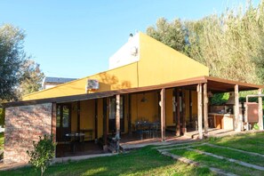 Ein gelbes Gebäude mit überdachter Veranda, Ziegelmauern und einem kleinen Garten.