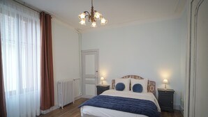 Een slaapkamer met een bed, twee nachtkastjes met lampen, een radiator, een deur en een raam met gordijnen.
