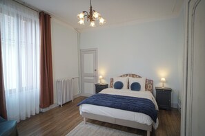 A bedroom with a bed, two bedside tables with lamps, a radiator, a door, and a window with curtains. - Gîte Saint Sauveur en Puisyae (Leugny)