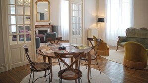 Een kamer met een ronde tafel, stoelen, een spiegel, een openhaard en een bank.