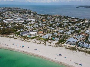 An aerial view of a coastal residential area with houses, a beach, and a clear view of the ocean. - Beautiful coastal home steps from beach with stunning Gulf views. (Holmes Beach)