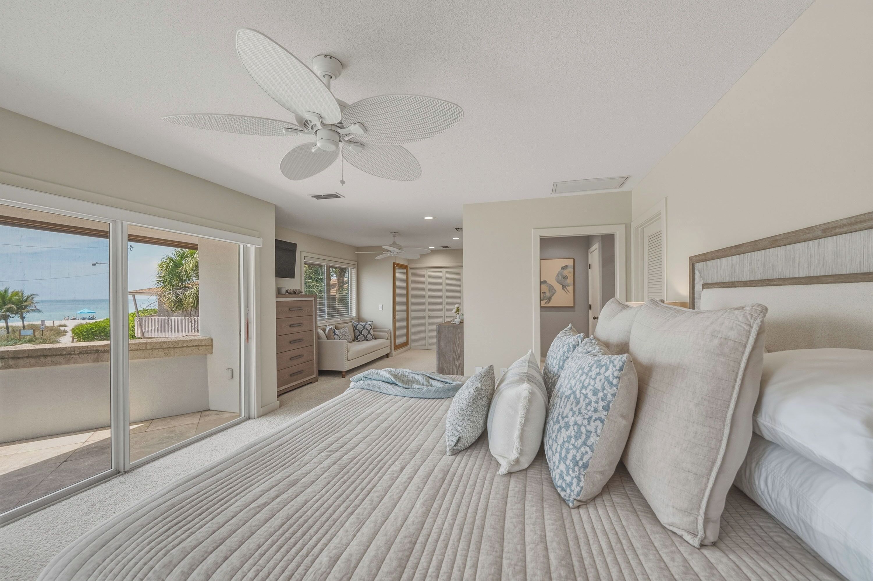 A bedroom with a large bed, a ceiling fan, a view of the ocean, and a sliding glass door leading to a balcony.