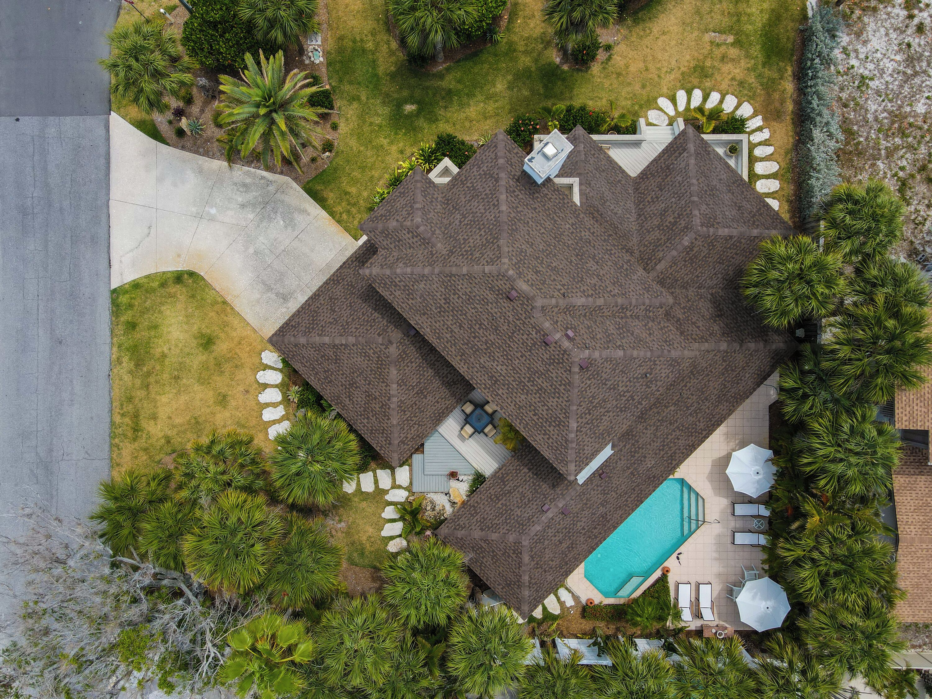 An aerial view of a house with a swimming pool, patio furniture, and surrounding greenery.