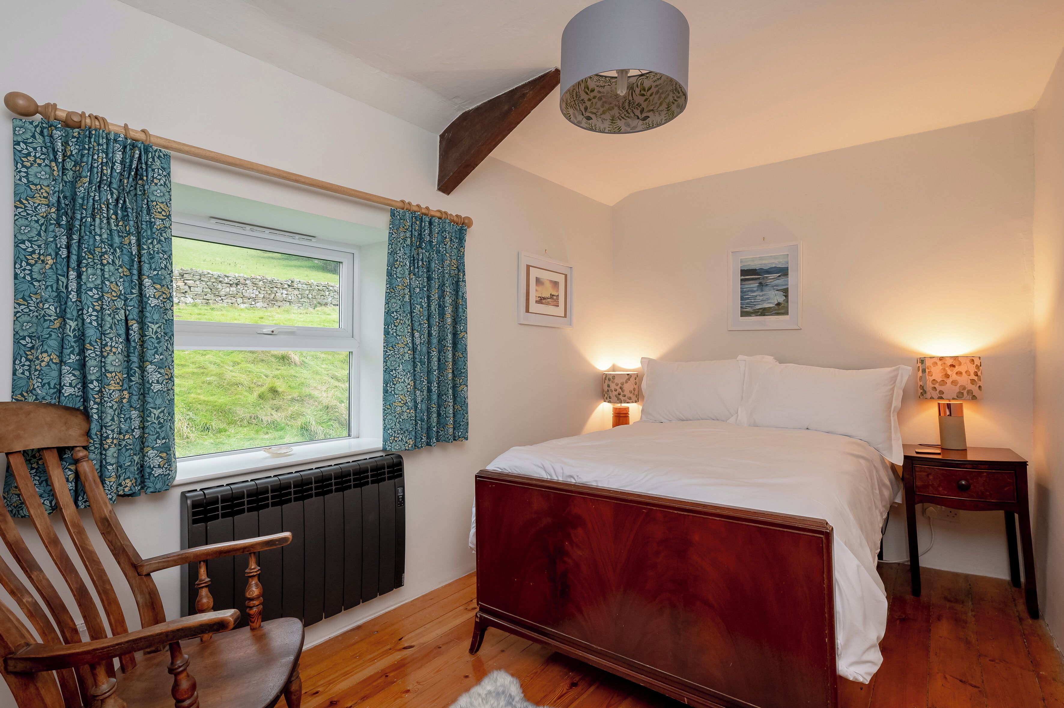 Une chambre à coucher avec un lit en bois, une chaise, une fenêtre avec des rideaux, deux lampes de chevet et un radiateur.