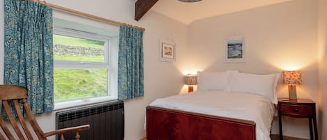 A bedroom with a wooden bed, a chair, a window with curtains, two bedside lamps, and a radiator.