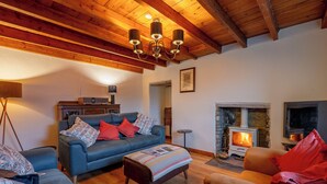 Ein gemütliches Wohnzimmer mit Kamin, einer Couch, einem Couchtisch und einer Holzzieldecke.