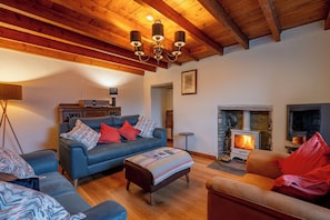 Ein gemütliches Wohnzimmer mit Kamin, einer Couch, einem Couchtisch und einer Holzzieldecke.