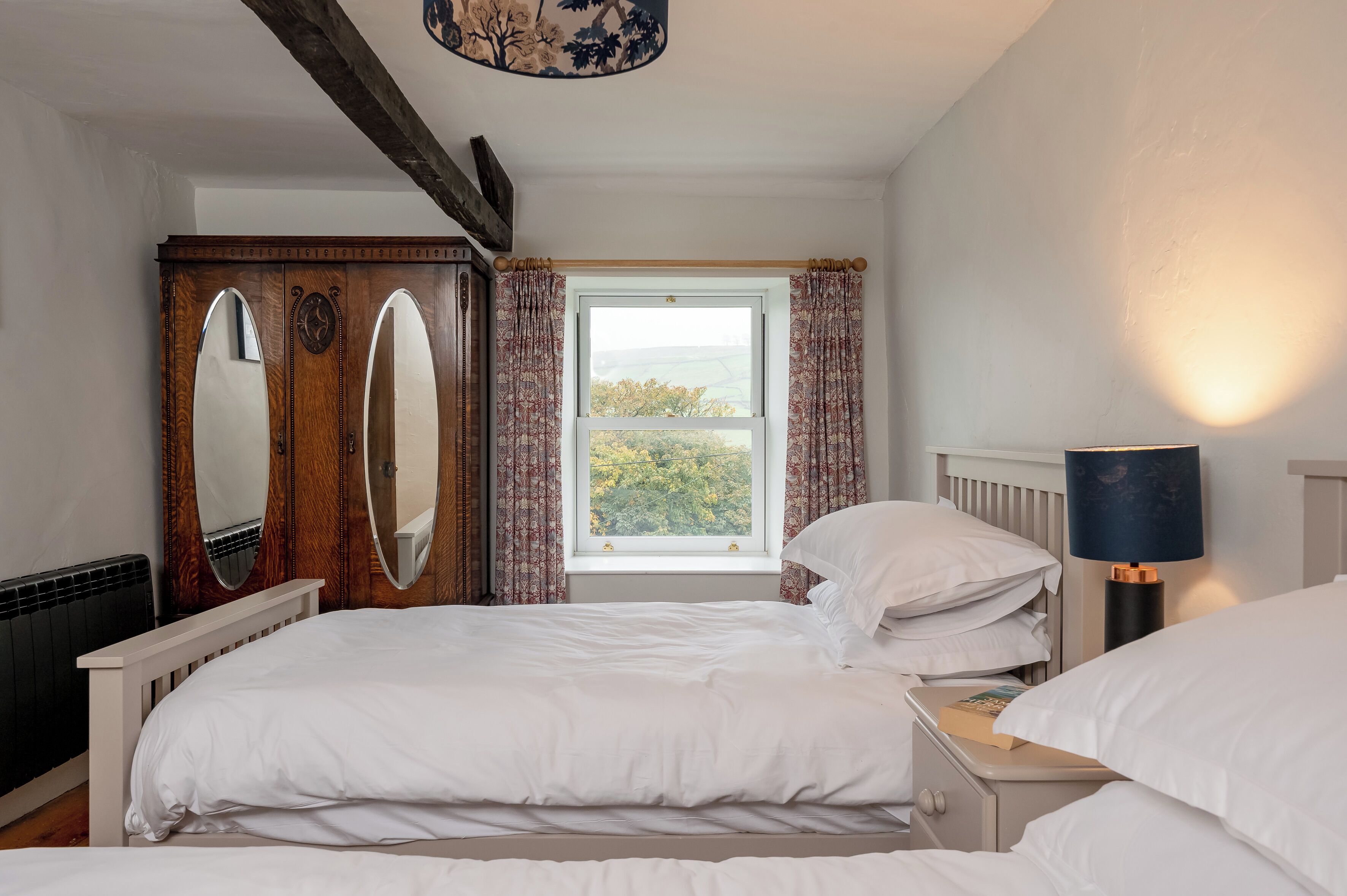 A bedroom with a bed, a nightstand, a lamp, a wardrobe, and a window with curtains.