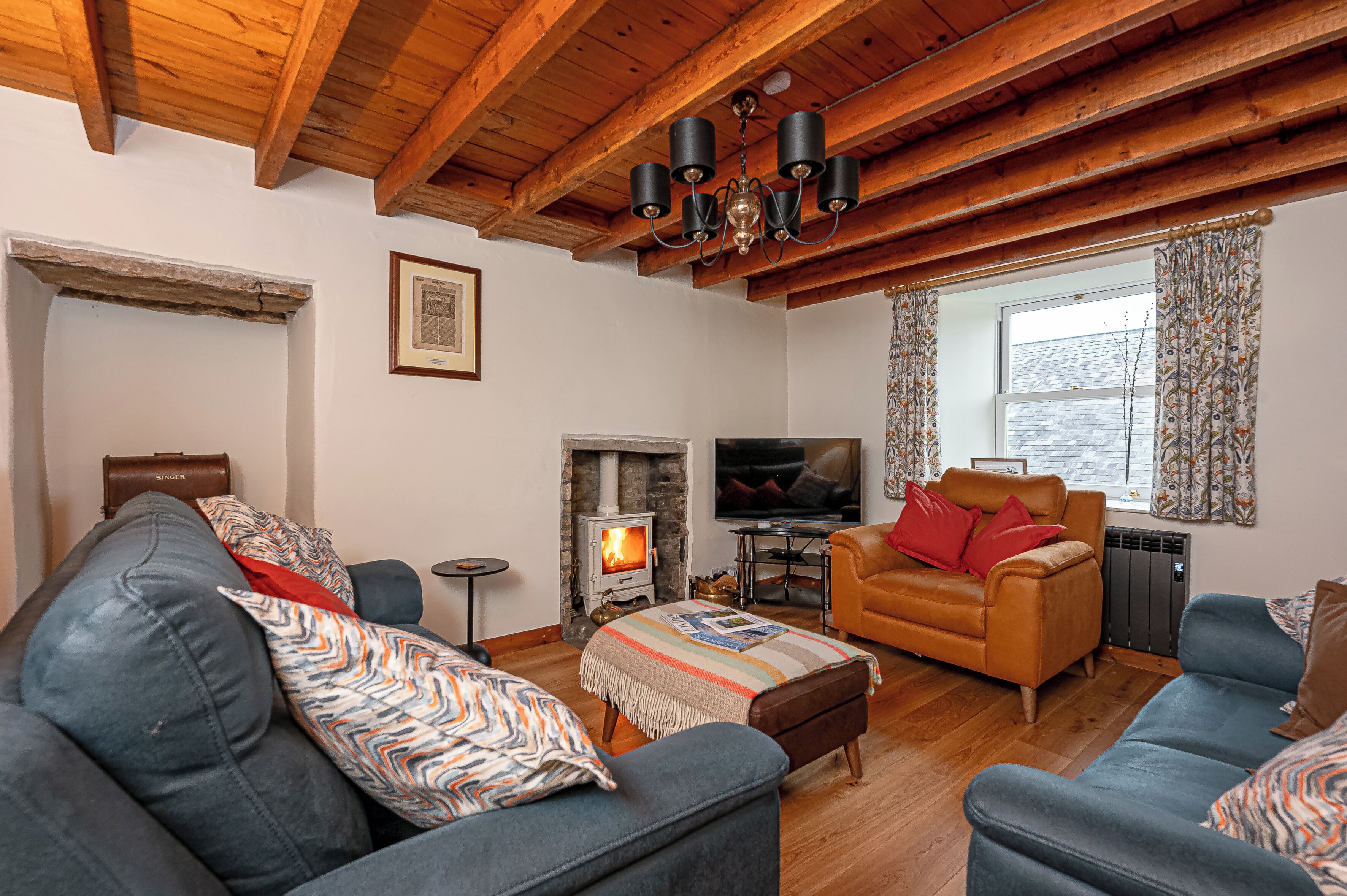 A cozy living room with a fireplace, leather sofas, a television, and wooden beams on the ceiling.