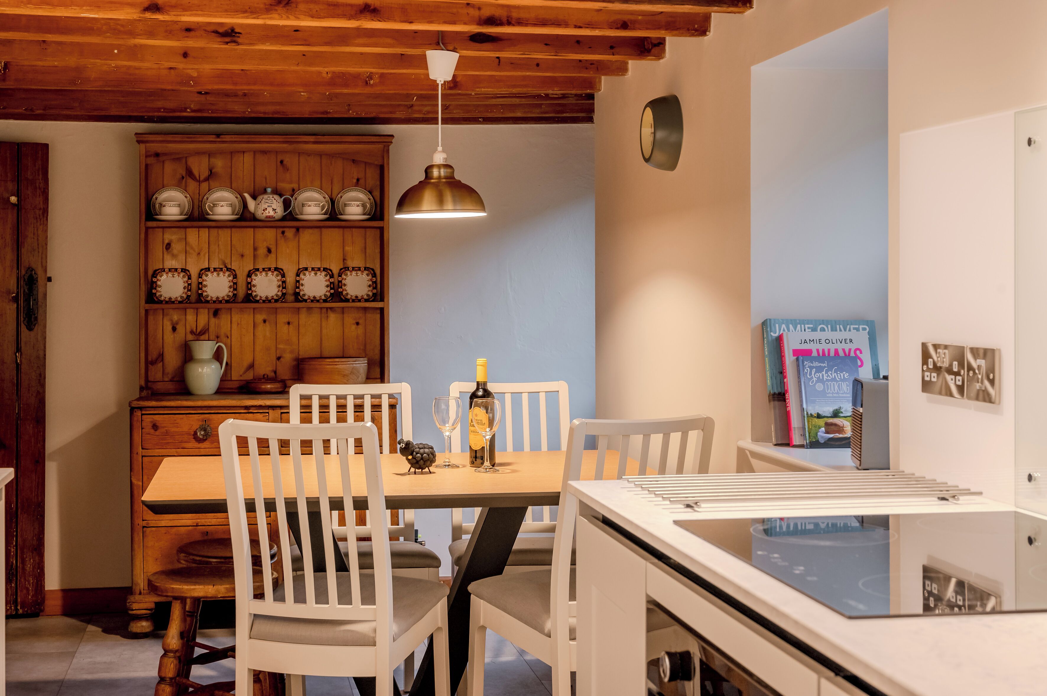 Et spiseområde med et træbord, hvide stole, en vinflaske og en bog med titlen 'Jamie Oliver'.