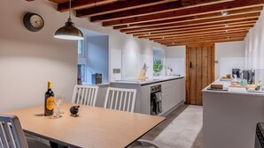 Eine moderne Küche mit Holzbalken, einem Essbereich mit Tisch, Stühlen und einer Weinflasche.