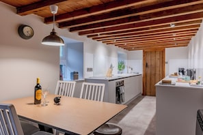 Eine moderne Küche mit Holzbalken, einem Essbereich mit Tisch, Stühlen und einer Weinflasche.